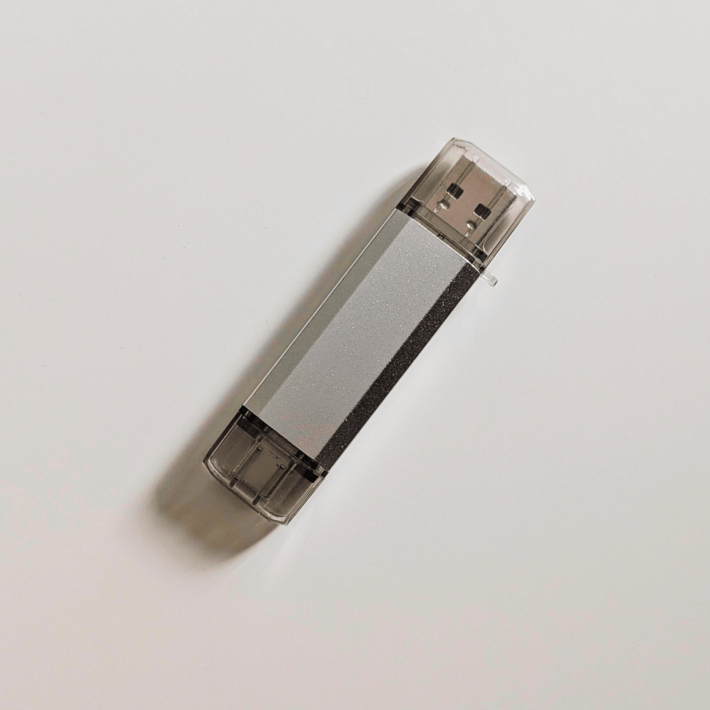 Srebrny BadUSB MalDuino W z wtykami USB-A i USB-C oraz przezroczystymi nakładkami ochronnymi, leżący na białym tle
