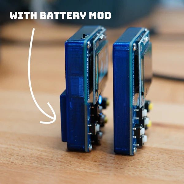 Two HackHeld Vega II devices in translucent blue cases standing side by side on a wooden surface - the left one with the Battery Mod has a thicker base and a WITH BATTERY MOD caption with a hand-drawn arrow, the right one without the mod is slimmer, yellow and white buttons are visible