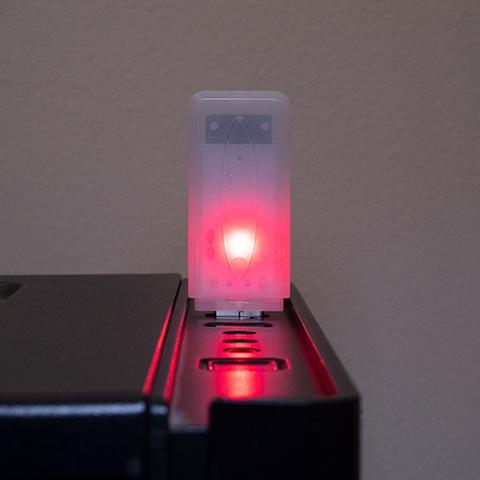 Urządzenie Deauth Detector w półprzezroczystej obudowie wpięte w port USB ze świecącą czerwoną diodą sygnalizującą wykrycie ataku deauthentication