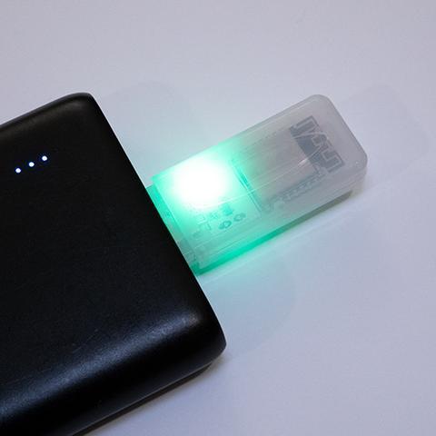 Urządzenie Deauth Detector w półprzezroczystej obudowie wpięte w port USB powerbanku ze świecącą zieloną diodą sygnalizującą brak ataku
