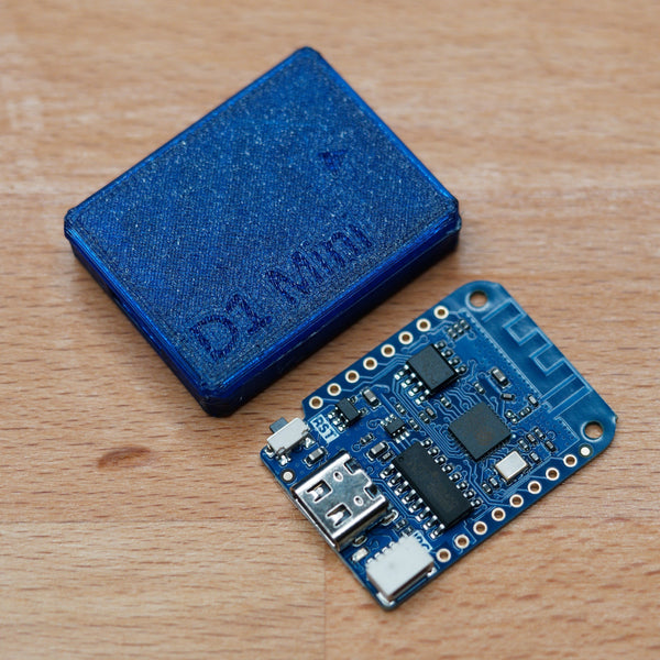 WiFi-деаутентификатор на плате D1 Mini (ESP8266) рядом с синим корпусом 3D-печати с тиснением D1 Mini - виден USB-разъём, чип ESP, дорожка WiFi-антенны и пины, на деревянной поверхности