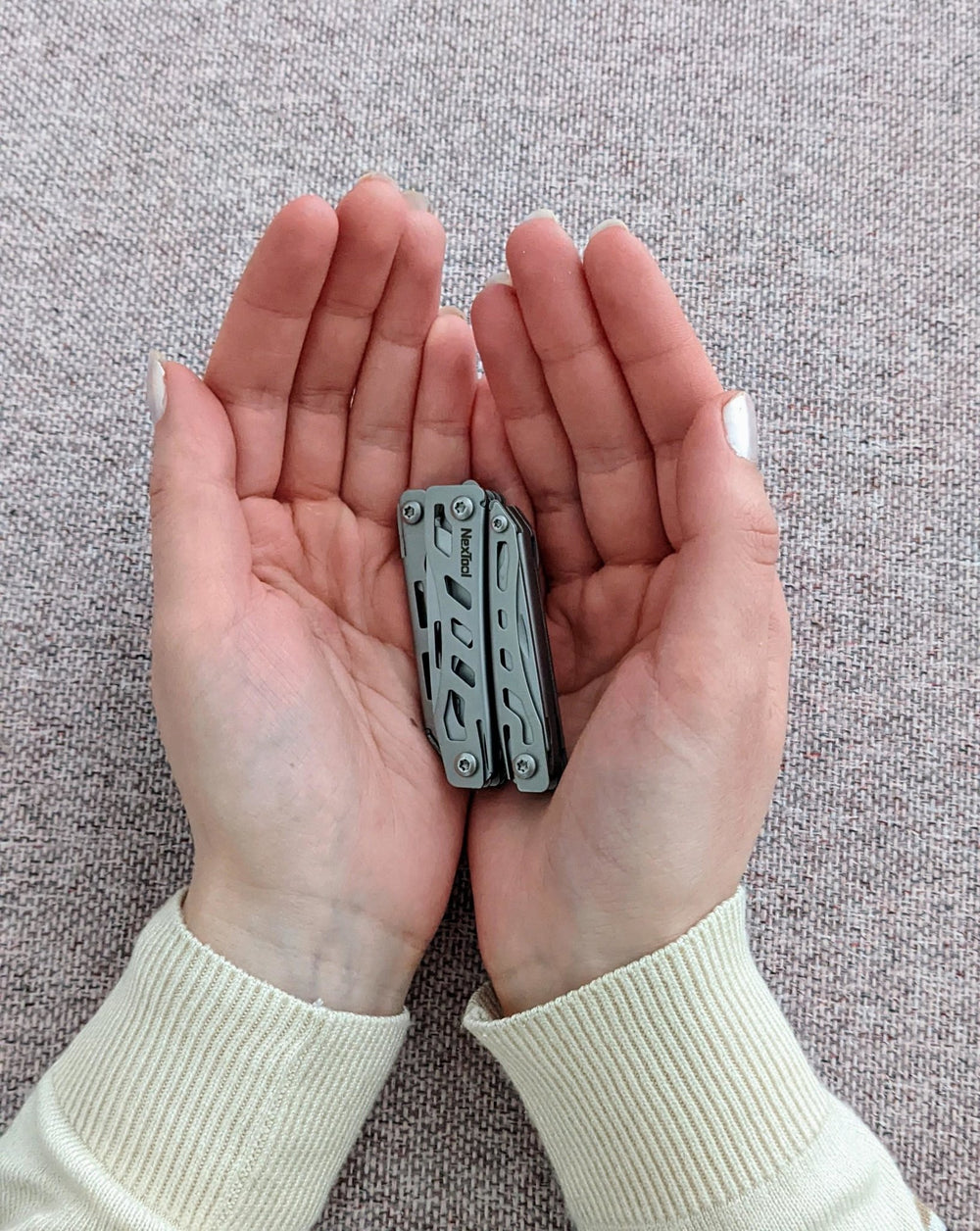 Złożony multitool NexTool Mini Flagship leżący na dwóch otwartych dłoniach, pokazujący niewielki rozmiar
