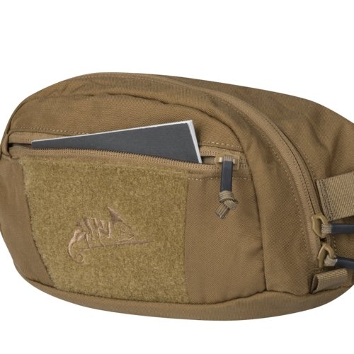 Helikon-Tex Bandicoot waist pack (coyote) - close-up of the front zippered pocket with a notebook inside, the velcro panel with the Helikon-Tex logo and zipper pulls, on white