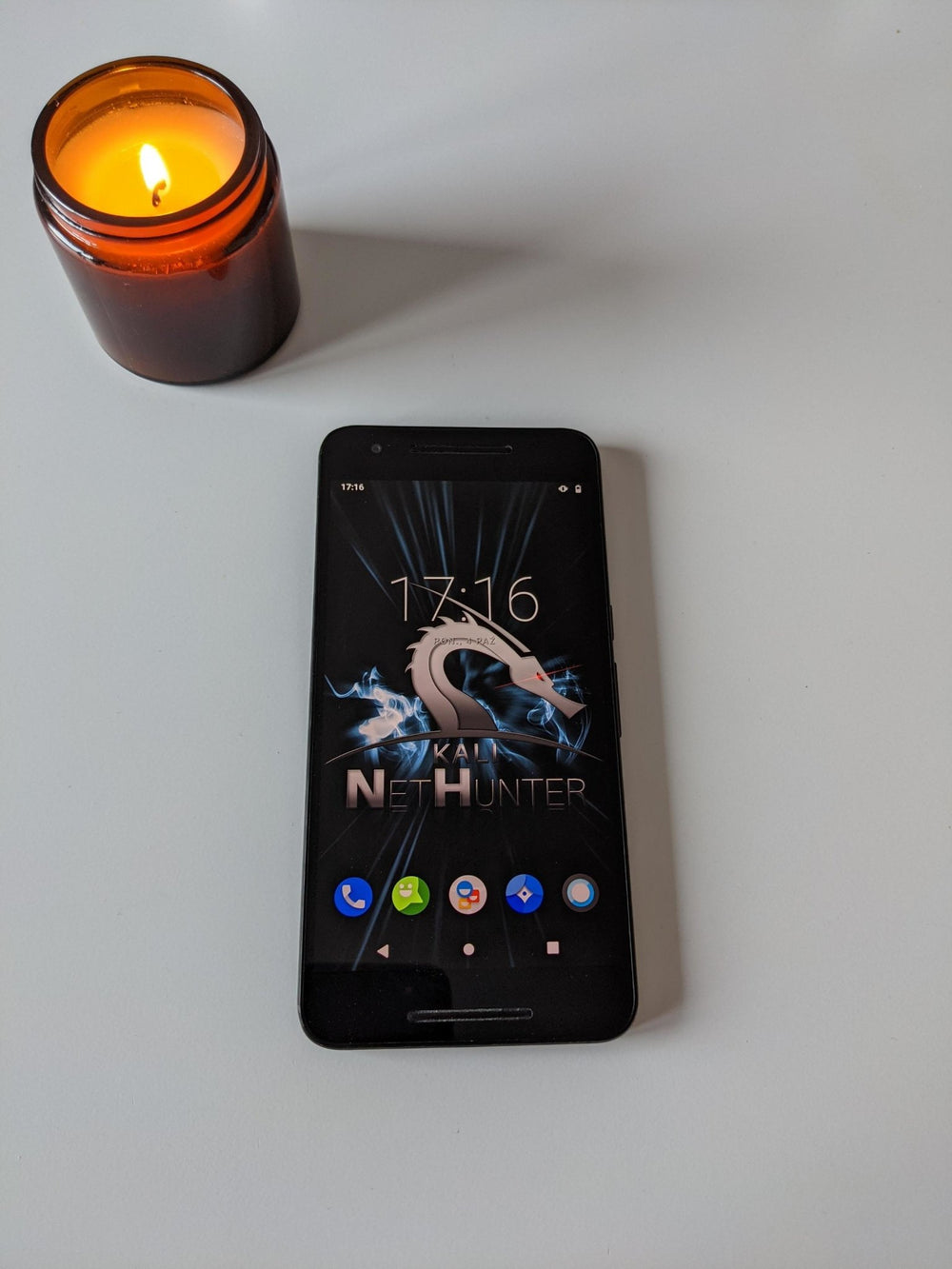 Czarny smartfon Nexus 6p z ekranem startowym Kali NetHunter (logo smoka i zegar) leżący obok zapalonej świecy