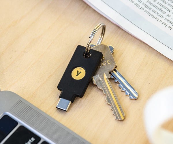 Schwarzer Yubico Security Key C NFC Sicherheitsschlüssel mit USB-C-Stecker an einem Bund Hausschlüssel, auf einem Schreibtisch neben einem Laptop liegend