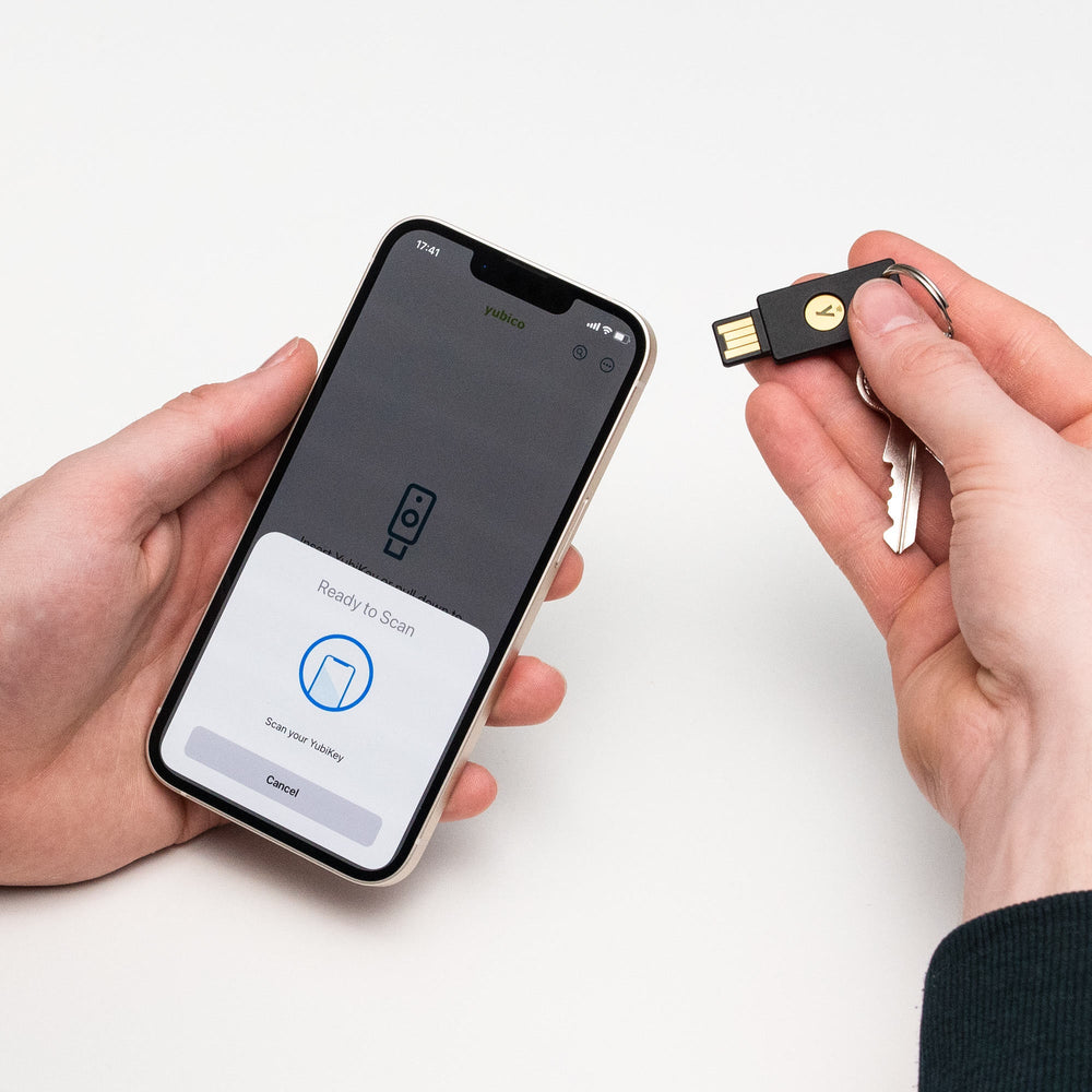 Scéna použití NFC - osoba drží černý klíč Yubico Security Key NFC vedle iPhonu s aplikací připravenou ke skenování