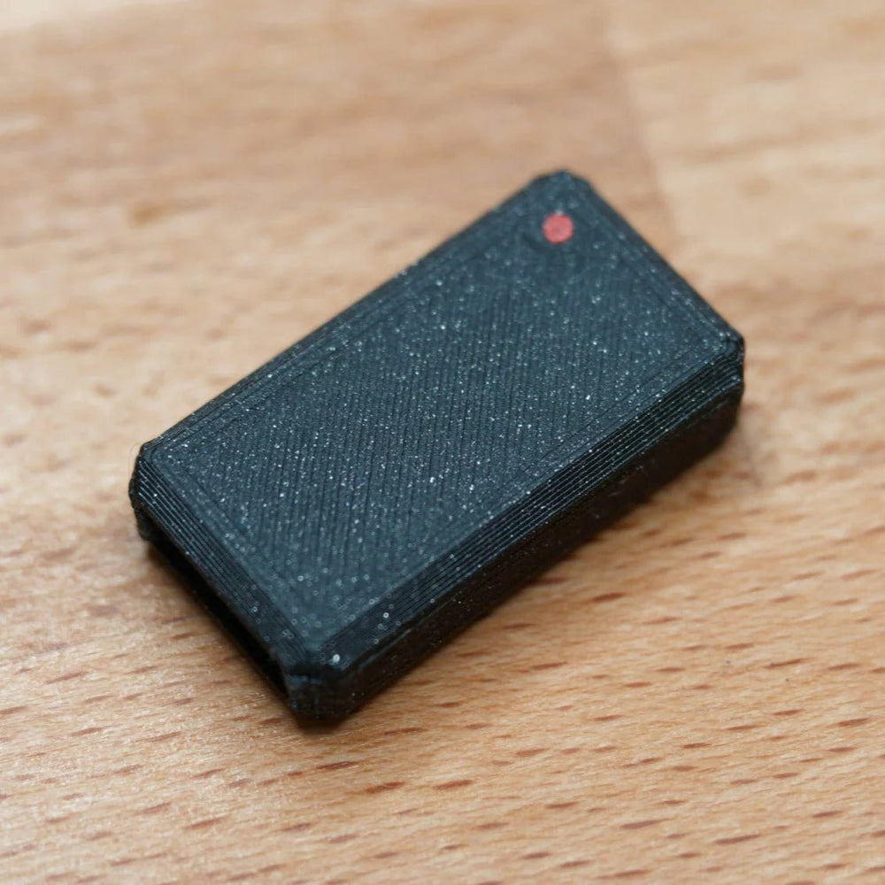 A single assembled black glittery USB Nova case with a red LED, on a wooden surface
