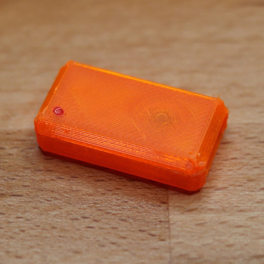 A single assembled orange USB Nova case with a red LED, on a wooden surface