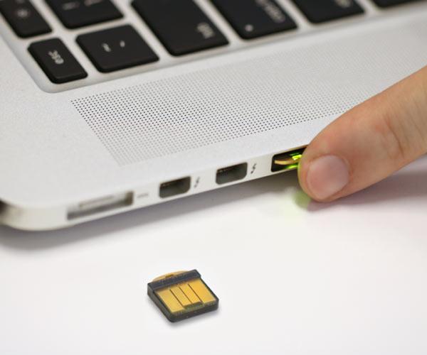 Сцена использования - маленький ключ YubiKey 5 Nano, вставленный в порт USB-A ноутбука, человек касается его пальцем для аутентификации, второй экземпляр рядом