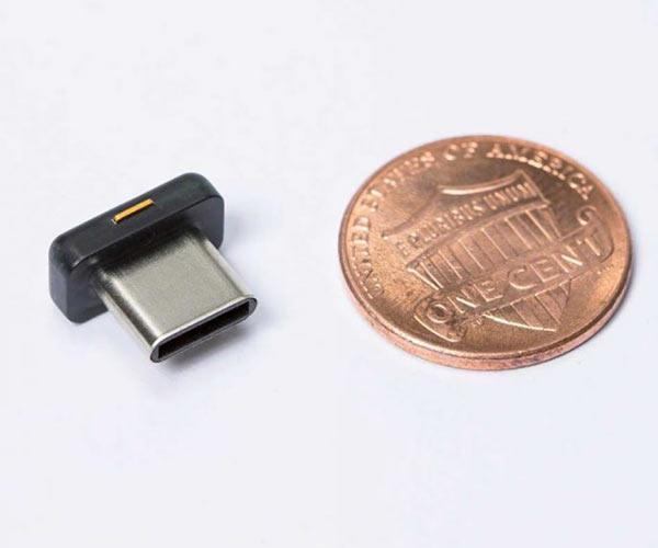 Mały czarny klucz YubiKey 5C Nano z wtykiem USB-C obok monety 1 cent, pokazuje kompaktowy rozmiar