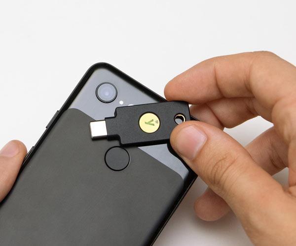 Сцена использования NFC - человек прикладывает чёрный ключ YubiKey 5C NFC к задней стороне смартфона для бесконтактной аутентификации
