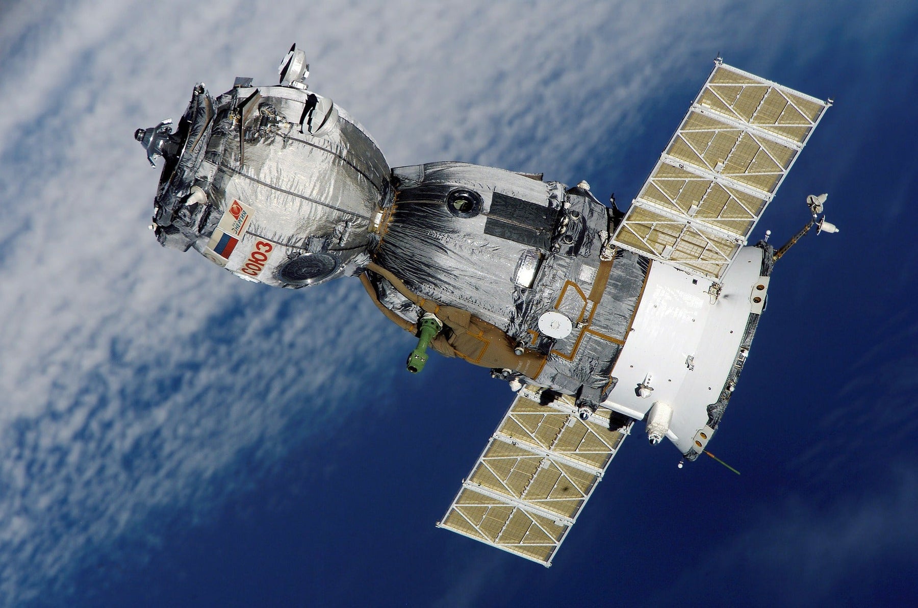 Sojus-Raumschiff mit ausgefahrenen Solarpaneelen im Orbit über der wolkigen blauen Erde