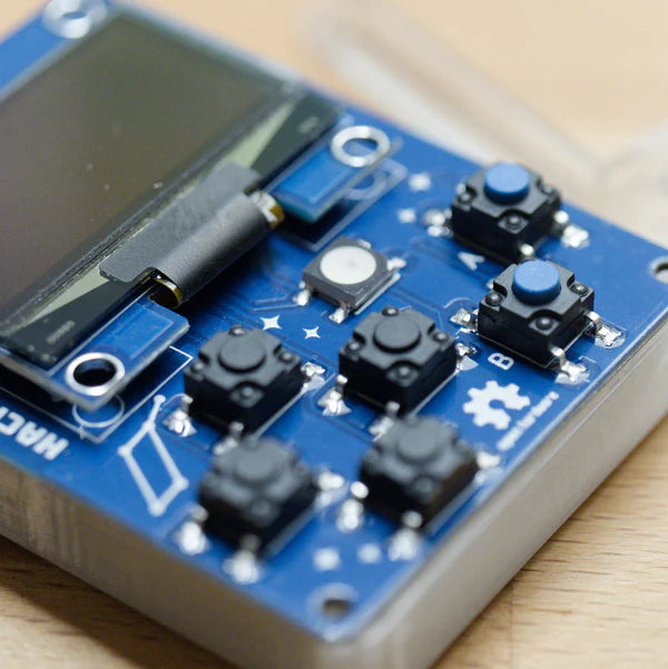 Makro płytki HackHeld Vega II+ - czarne przyciski w układzie krzyżaka oraz niebieskie przyciski A i B, krawędź wyświetlacza OLED, przycisk reset i logo Spacehuhn na niebieskiej płytce w przezroczystej obudowie, na drewnie