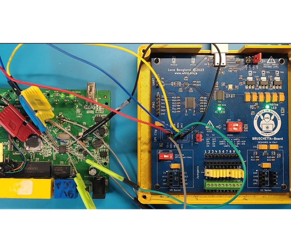 BRUSCHETTA-Board in a yellow case wired with clip leads to a target board on a blue background, the IC LED lit green