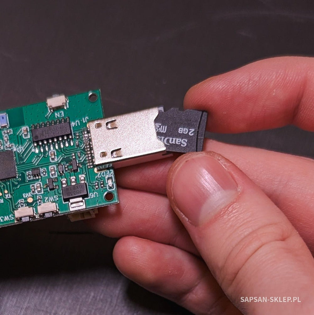 Evil Crow RF V2 board held in hand with a SanDisk 2 GB microSD card being inserted into the slot next to the USB connector