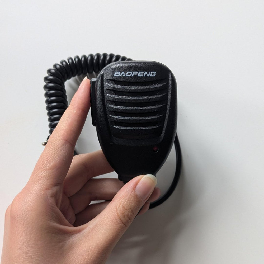Czarny mikrofonogłośnik Baofeng trzymany w dłoni, z kratką głośnika, logo i bocznym przyciskiem PTT