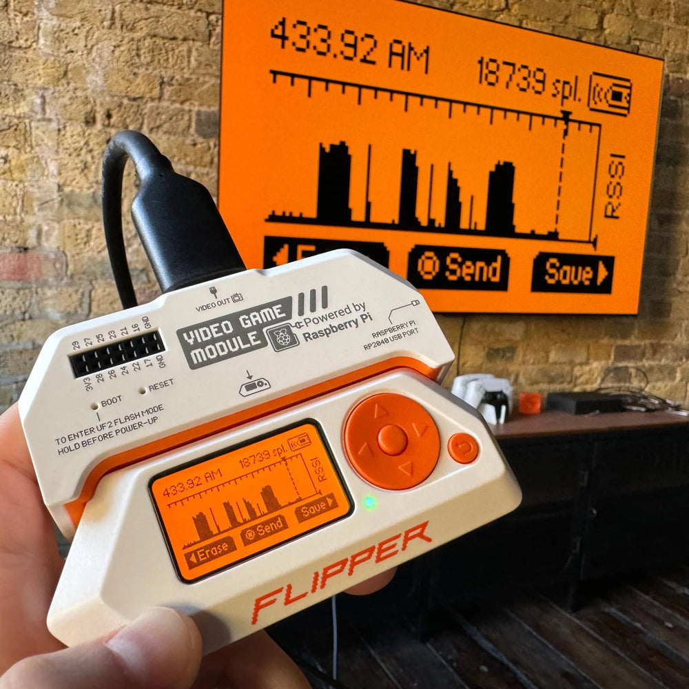 Flipper Zero с игровым видеомодулем RP2040 в руке, приём SubGHz 433.92 МГц показан на большом экране на кирпичной стене