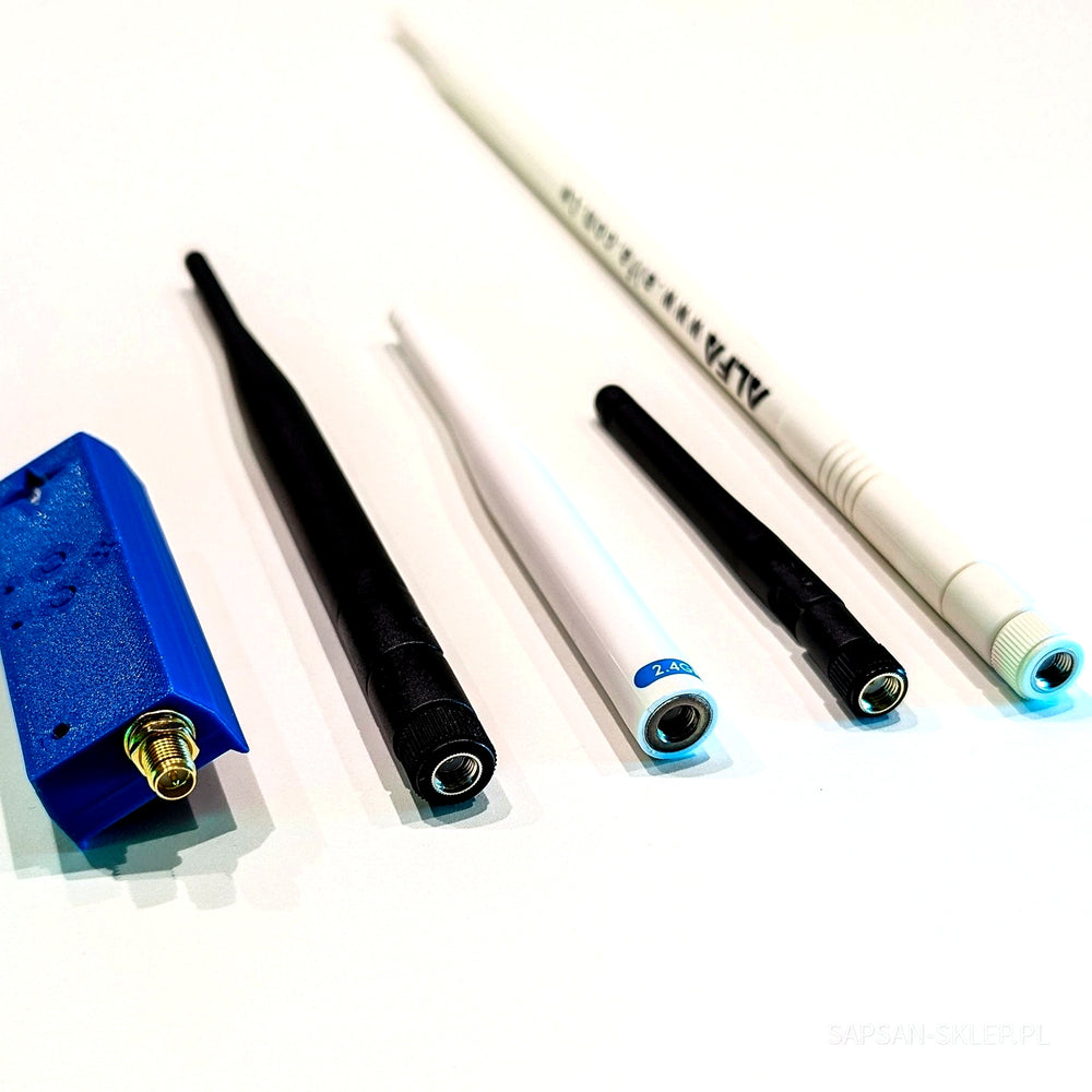 Blue NetNinja module with the S logo and a gold SMA connector next to four unscrewed antennas of different lengths on a white background - a black antenna, a thin white antenna marked 2.4G, a shorter black antenna and a long white ALFA antenna, SAPSAN-SKLEP.PL watermark