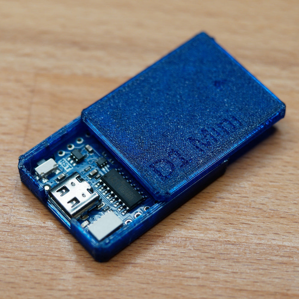 Tester WiFi D1 Mini w przezroczystej niebieskiej obudowie druku 3D z napisem D1 Mini, pokrywa odsunięta - widać płytkę z gniazdem USB i układem w środku, na drewnie