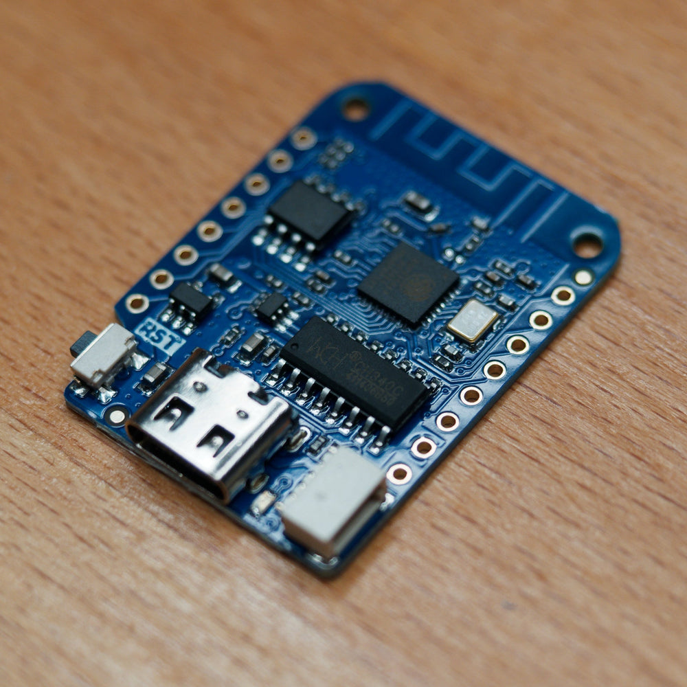 Zbliżenie płytki WeMos D1 Mini (ESP8266) - gniazdo USB-C, układ ESP8266, kość pamięci flash, konwerter CH340C, ścieżka anteny WiFi, przycisk RST i piny GPIO, na drewnie