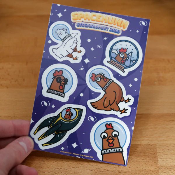 Spacehuhn sticker sheet held in a hand above a wooden surface