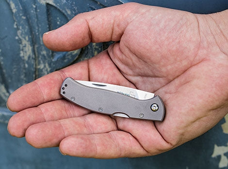 Lifestyle photo - a hand holding the folded Böker Plus Titan Drop knife with a grey titanium handle, showing its size