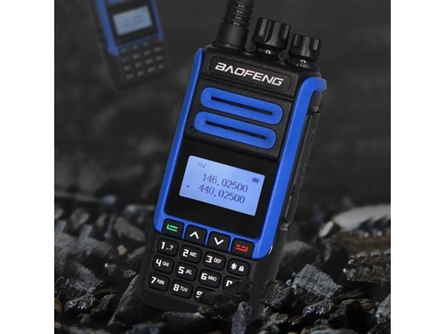 Baofeng BF-H7 10W radio in a styled shot - the black-and-blue radio with an antenna and LCD display standing on dark rocky ground, with a second blurred radio in the background, a dark background
