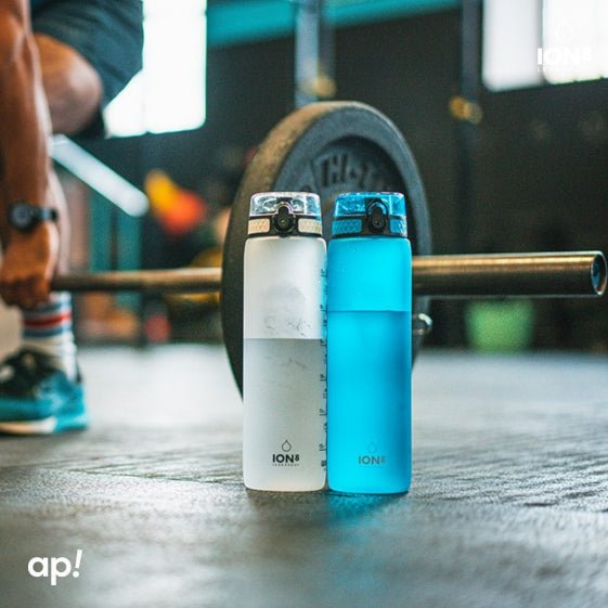 Two ION8 water bottles - clear and blue - standing next to a loaded barbell in a gym, lifestyle shot
