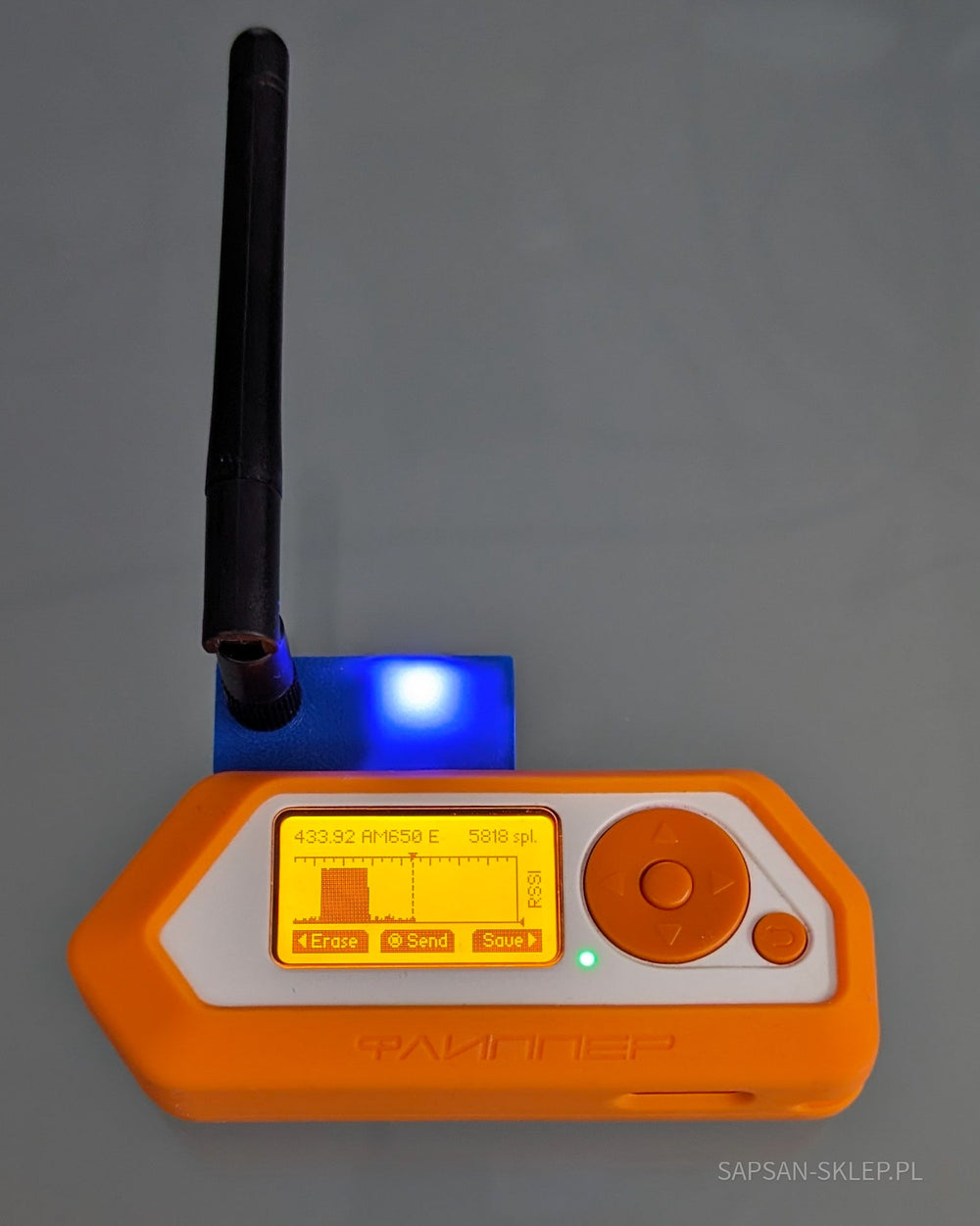 Externí modul CC1101 nasazený na oranžový Flipper Zero na šedém pozadí - modré pouzdro tištěné 3D s černou anténou a svítící modrou LED, na obrazovce zachycený sub-GHz signál 433.92 AM650 E 5818 spl. s grafem vlny, popiskem RSSI a nabídkou Erase, Send, Save, vodoznak SAPSAN-SKLEP.PL