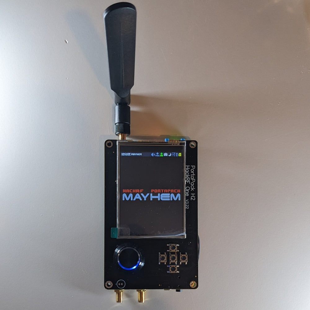 Černé zařízení HackRF One s nástavbou PortaPack H2 a úvodní obrazovkou firmwaru Mayhem, s připojenou anténou a kolečkem