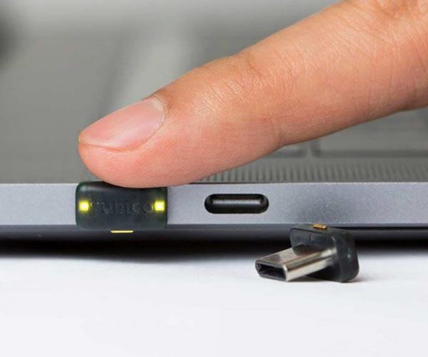 Mały klucz YubiKey 5C Nano wpięty w port USB-C laptopa, osoba dotyka złotego styku do uwierzytelnienia