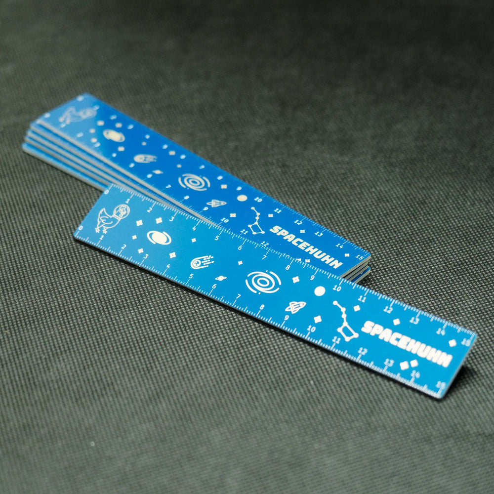 Několik modrých PCB pravítek Spacehuhn naskládaných na sobě, s plnou stupnicí 15 cm a vesmírnou grafikou