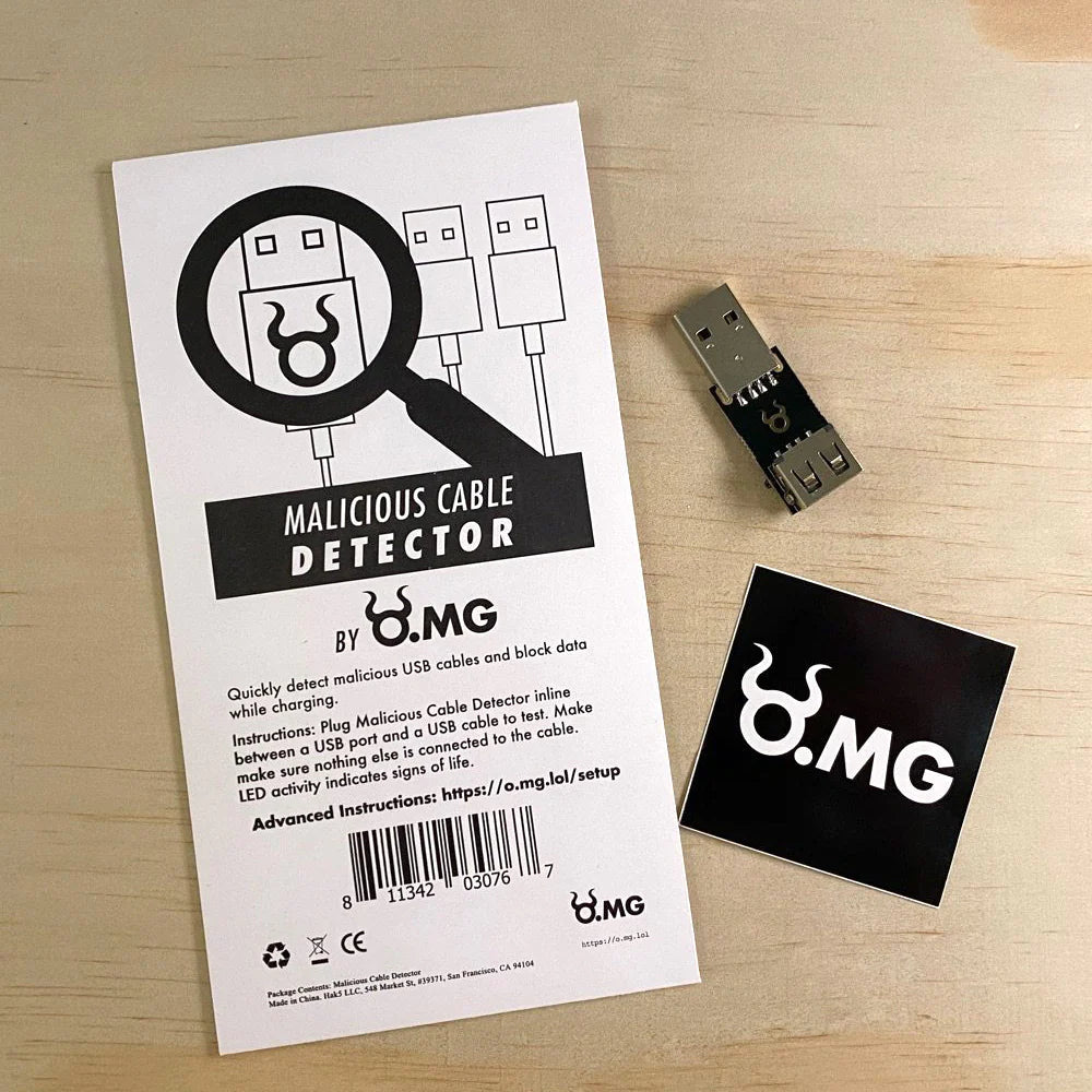Obsah sady detektoru škodlivých kabelů O.MG na dřevěné desce - bílá karta s grafikou lupy nad USB konektorem a nápisem MALICIOUS CABLE DETECTOR BY O.MG, samotné USB zařízení a černá samolepka s logem O.MG