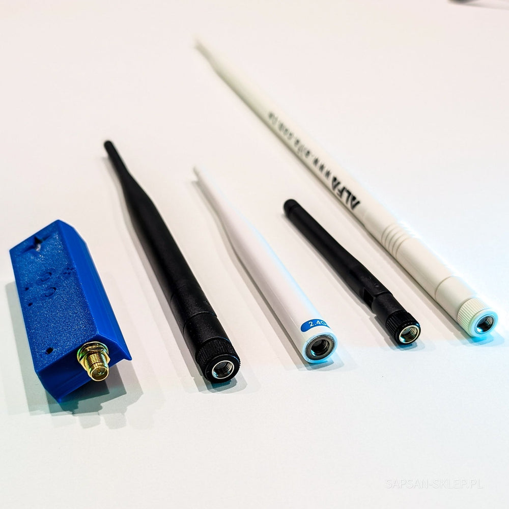 Blaues NetNinja-Modul mit einem S-Logo und einem goldenen SMA-Anschluss neben vier abgeschraubten Antennen unterschiedlicher Länge auf weißem Hintergrund - eine schwarze Antenne, eine dünne weiße Antenne mit der Aufschrift 2.4G, eine kürzere schwarze Antenne und eine lange weiße ALFA-Antenne, das SAPSAN-SKLEP.PL-Wasserzeichen