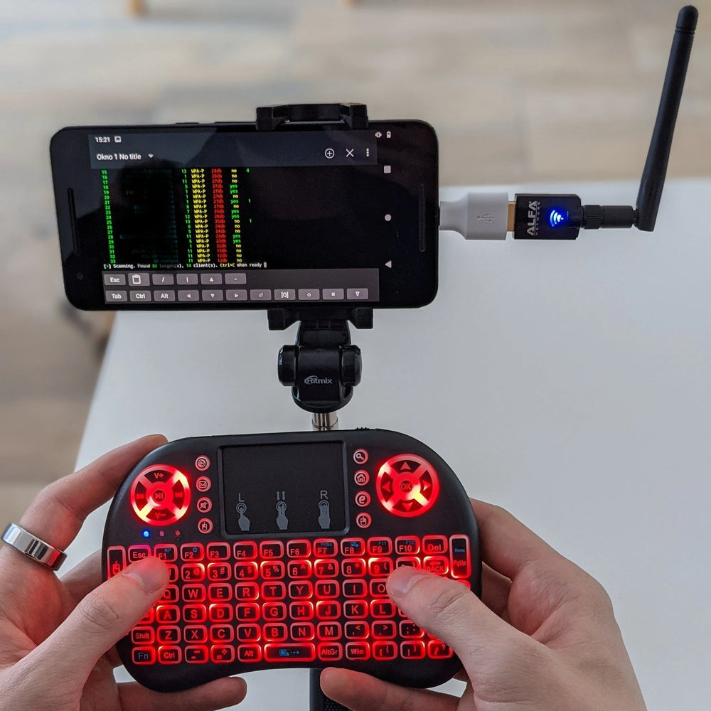 Scena użycia - smartfon Nexus 6p na statywie z terminalem Kali NetHunter skanującym sieci WiFi, podłączony adapter ALFA z anteną oraz dłonie na podświetlanej mini klawiaturze