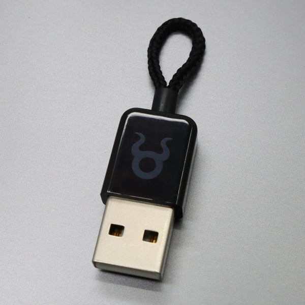 O.MG Plug od Hak5 - černé zařízení s konektorem USB-A vypadající jako běžná USB koncovka, s nenápadným logem býka O.MG a pleteným černým poutkem, na šedém pozadí