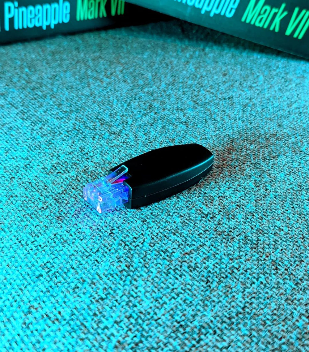 Hak5 Shark Jack ze świecącym na niebiesko złączem Ethernet, leżący na turkusowej tkaninie, w tle pudełko WiFi Pineapple