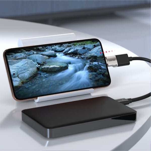 Adapter Unitek łączący smartfon przez USB-C z zewnętrznym dyskiem, w tle telefon na podstawce z filmem