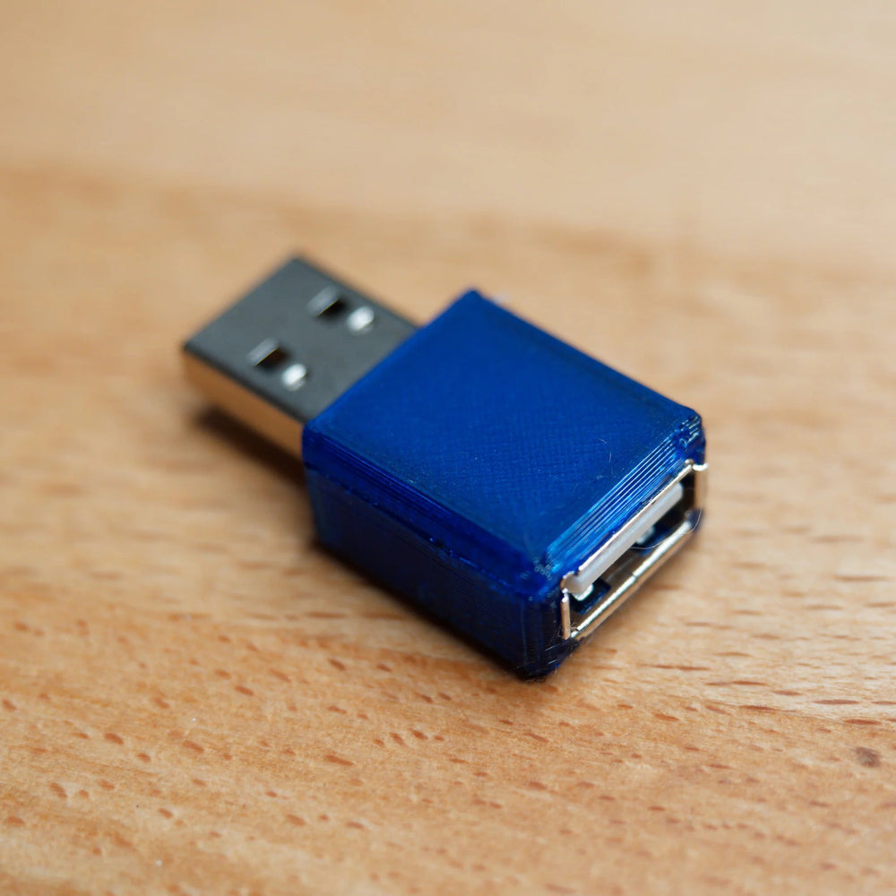 USB blokátor dat v průhledném modrém pouzdře - z jedné strany konektor USB-A, z druhé zásuvka USB-A, na dřevěné desce