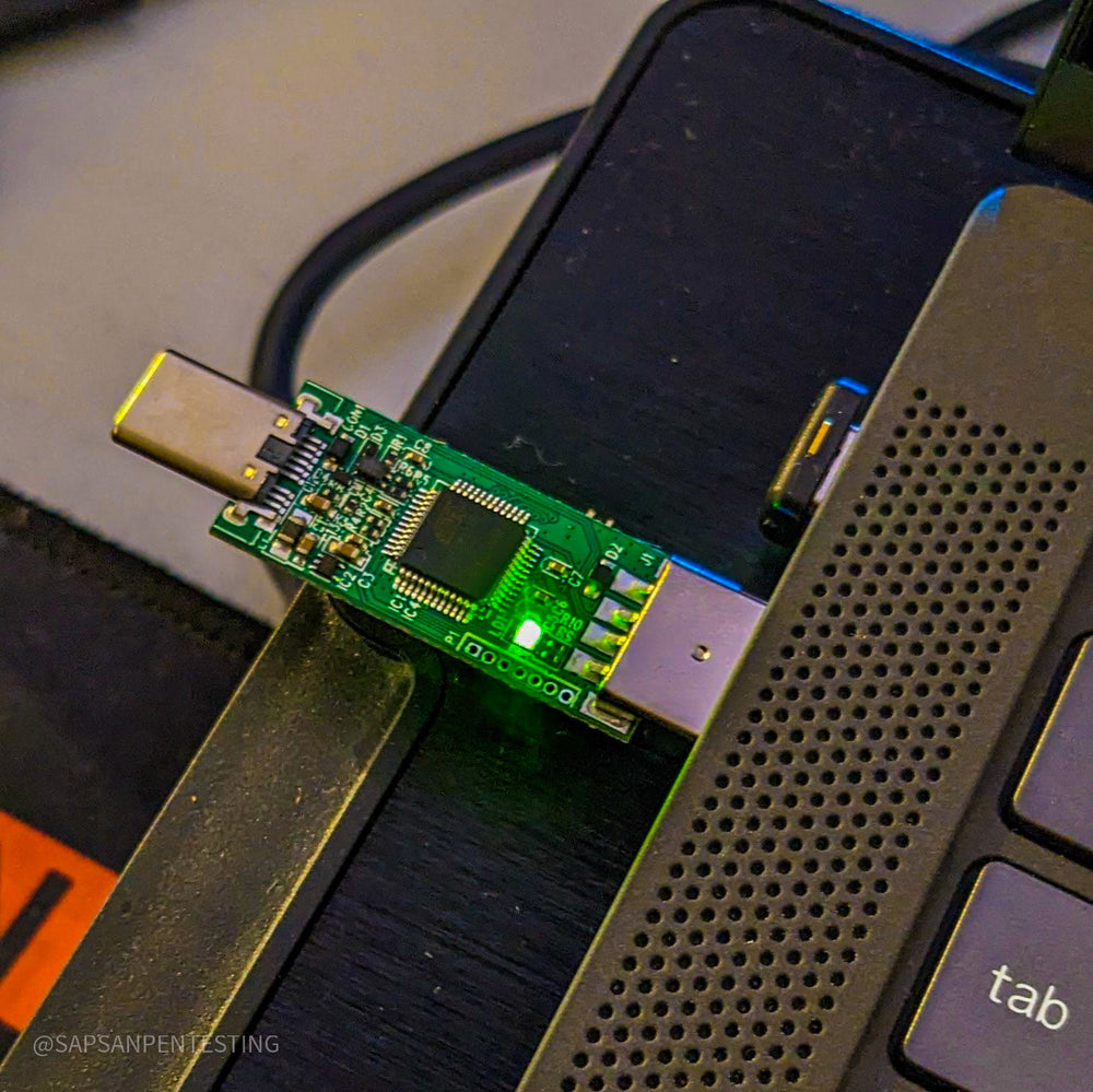 USB Rubber Ducky V2 от Hak5 - плата, вставленная в USB-порт ноутбука под углом, светящийся зелёный светодиод и видимый разъём USB-C, клавиатура позади