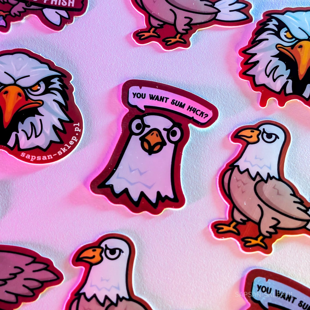 Close-up of the SAPSAN stickers in pink-magenta lighting - die-cut stickers with the eagle mascots, including an angry eagle head with the sapsan-sklep.pl text, an eagle with a YOU WANT SUM H4CK speech bubble and a standing eagle, the SAPSAN-SKLEP.PL watermark