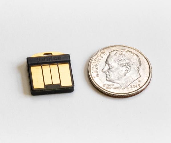 Маленький чёрный ключ YubiKey 5 Nano со штекером USB-A рядом с монетой 10 центов, показывает компактный размер