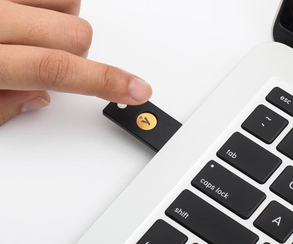 YubiKey 5 NFC plugged into a laptop's USB-A port, a person touching the gold button to authenticate