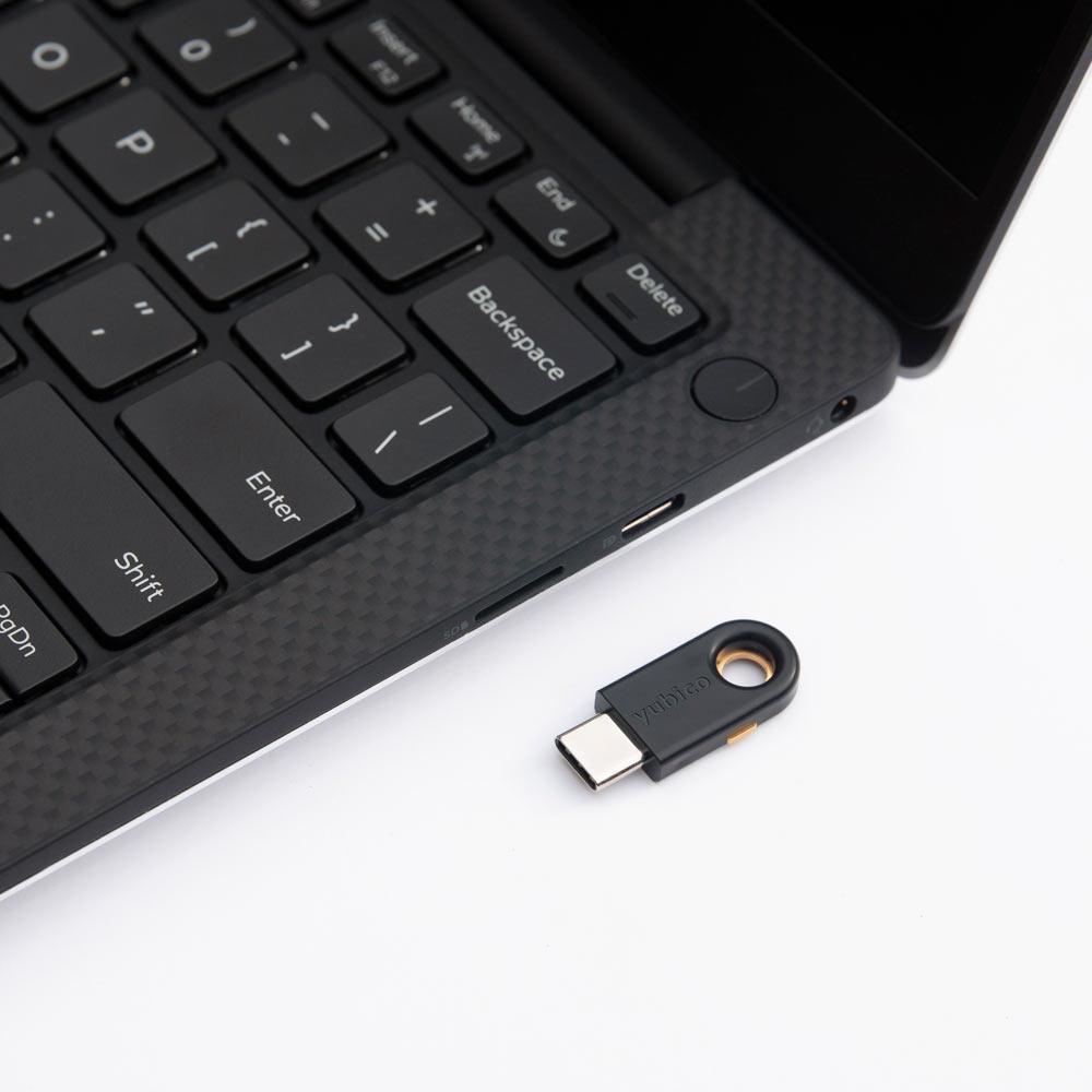 Schwarzer YubiKey 5C mit USB-C-Stecker neben einem Laptop, bereit zum Anschließen, yubico-Schriftzug